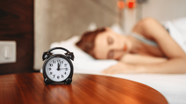 Alarm clock on a table in front of a woman getting 6 hours of sleep