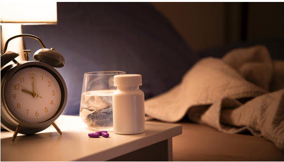 Bedside table with pills, a glass of water, and an alarm clock for the best time to go to bed