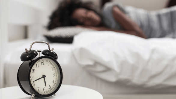 Closeup of an alarm clock near a woman sleeping with sciatica pain