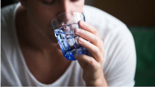 A man drinking a glass of water due to experiencing dehydration and blood pressure problems